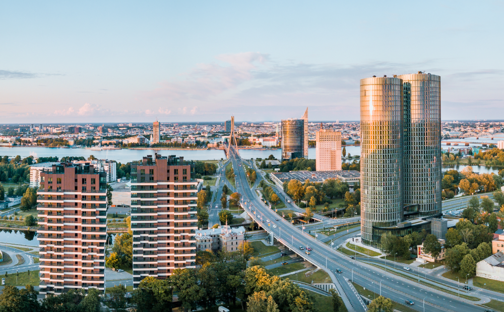 Aerial view of modern buildings and bridge in Riga, Latvia, during sunset with the Daugava River in the background.