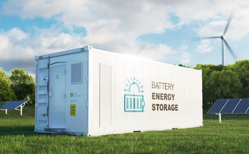 Battery energy storage container in a renewable energy field with solar panels and a wind turbine in the background.